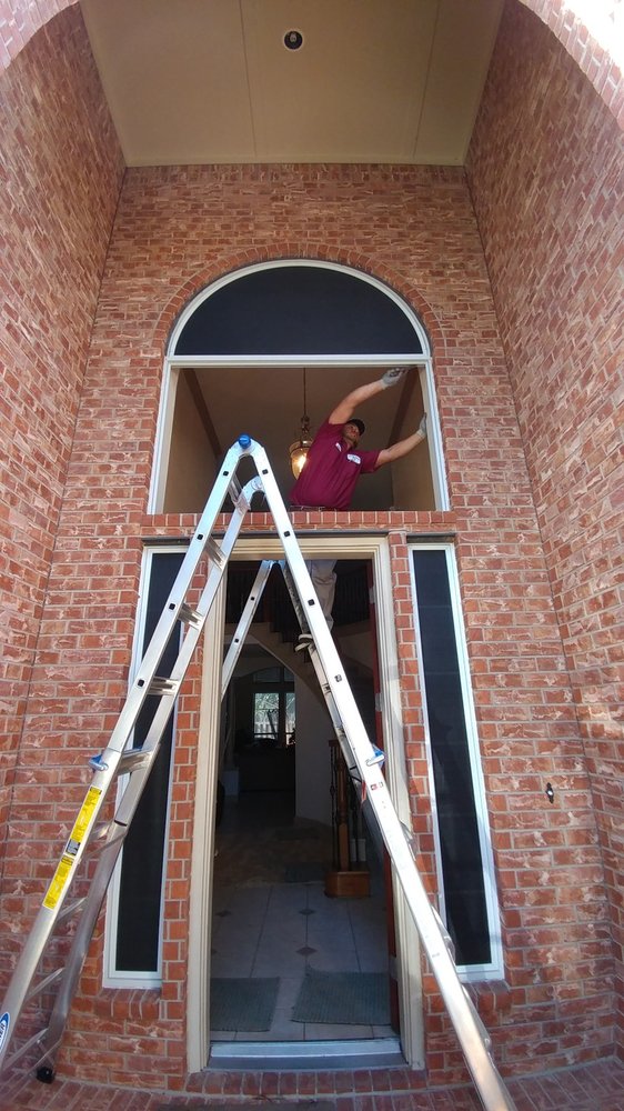 Installer on a ladder fitting glass above a two-story entryway